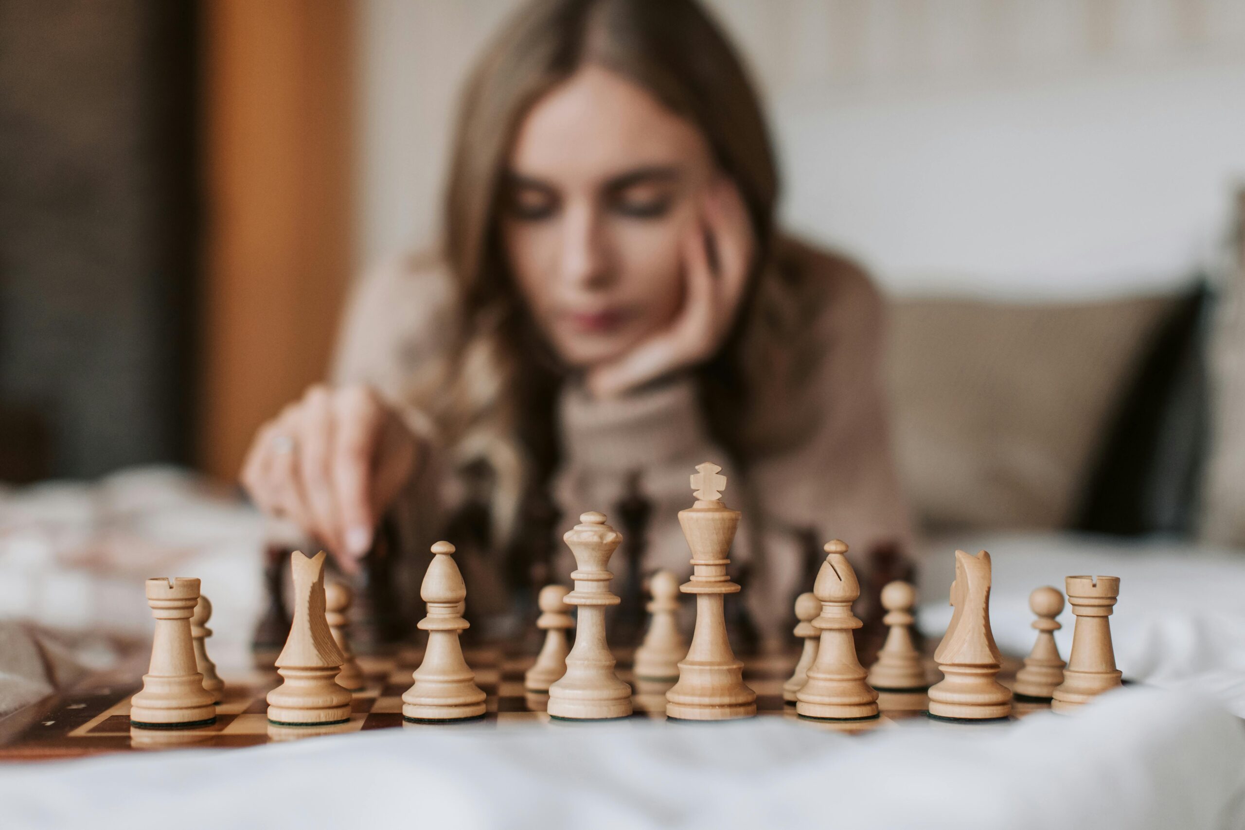 Focused woman engages in a thoughtful chess match, planning her next move on a wooden board.